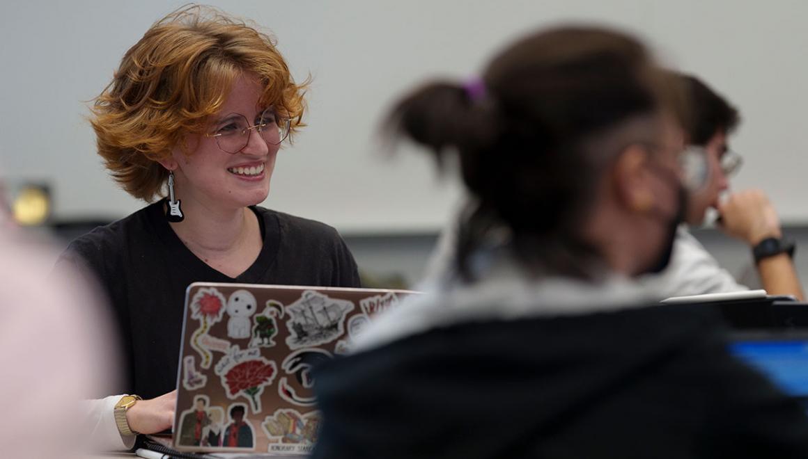 A Simmons graduate student seated in a classroom with a laptop open on the desk