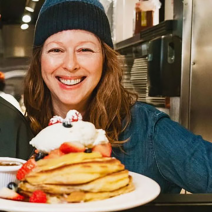 Dede Lehman smiling as she holds a plate full of pancakes