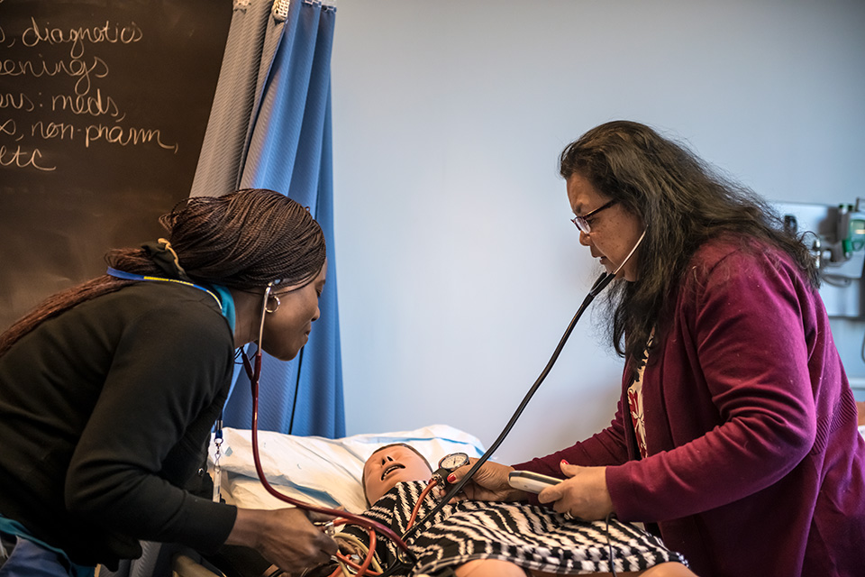 Two nursing students perform an exam on a nursing mannequin