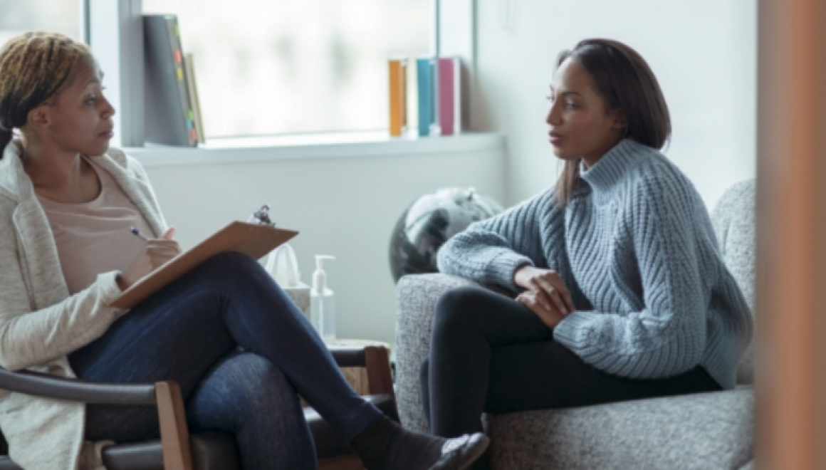 Two women sitting in chairs having a discussion.  One woman is holding a clipboard.