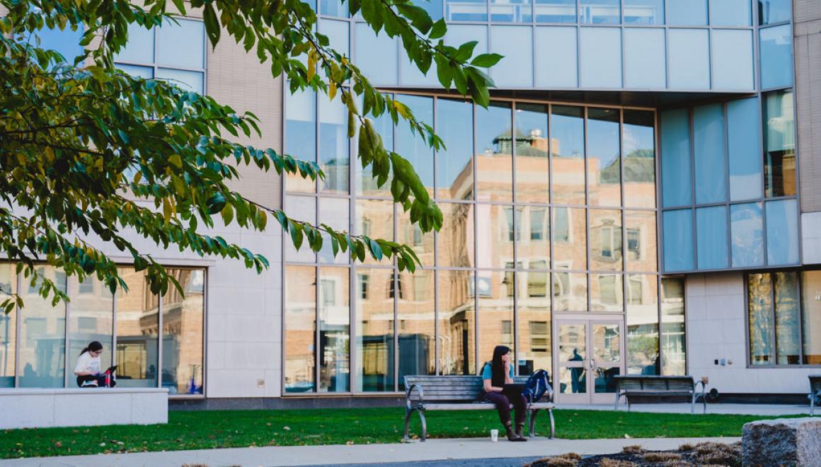 A student sits on a bench outside a building on the Simmons University campus