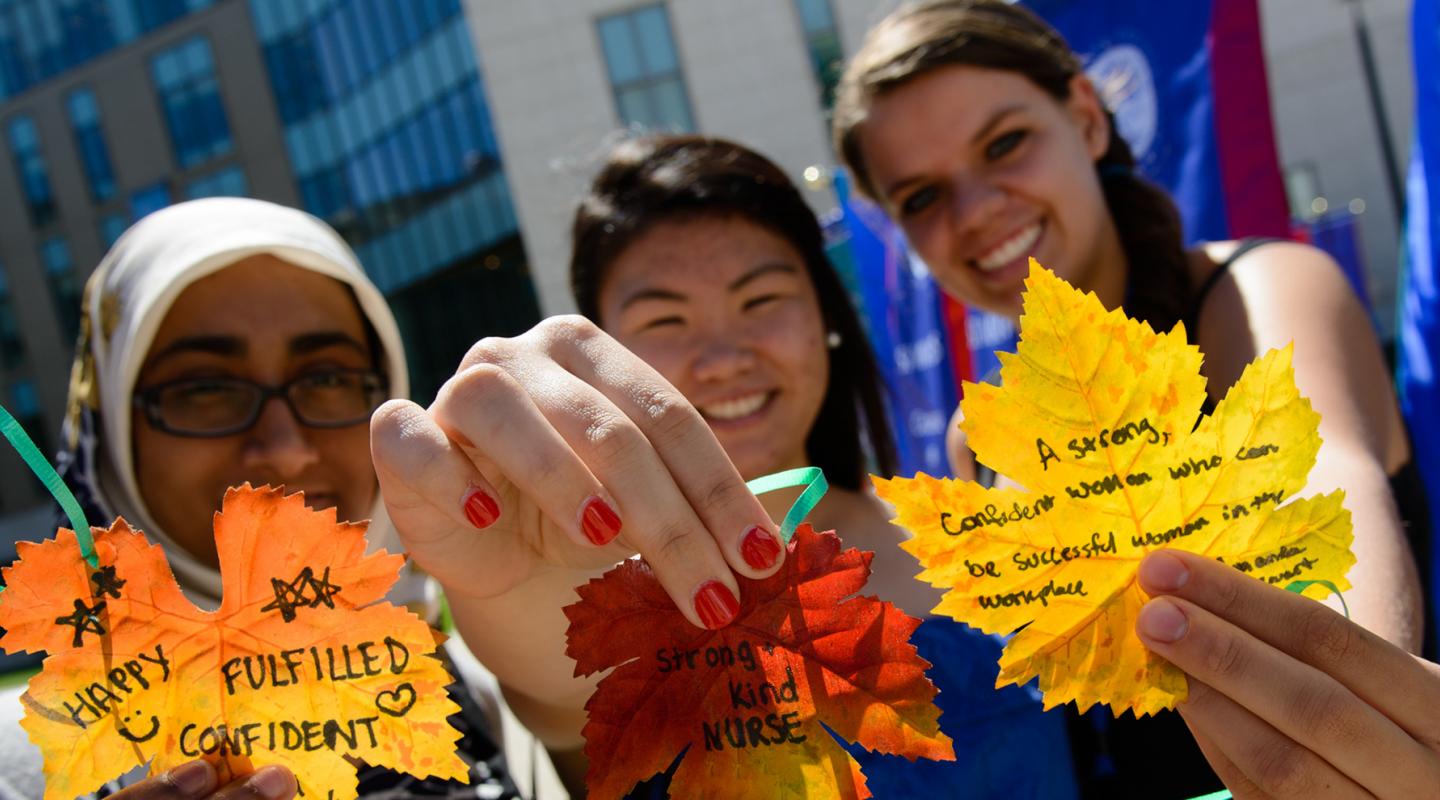 Student displaying leaves with messages of why they love Simmons