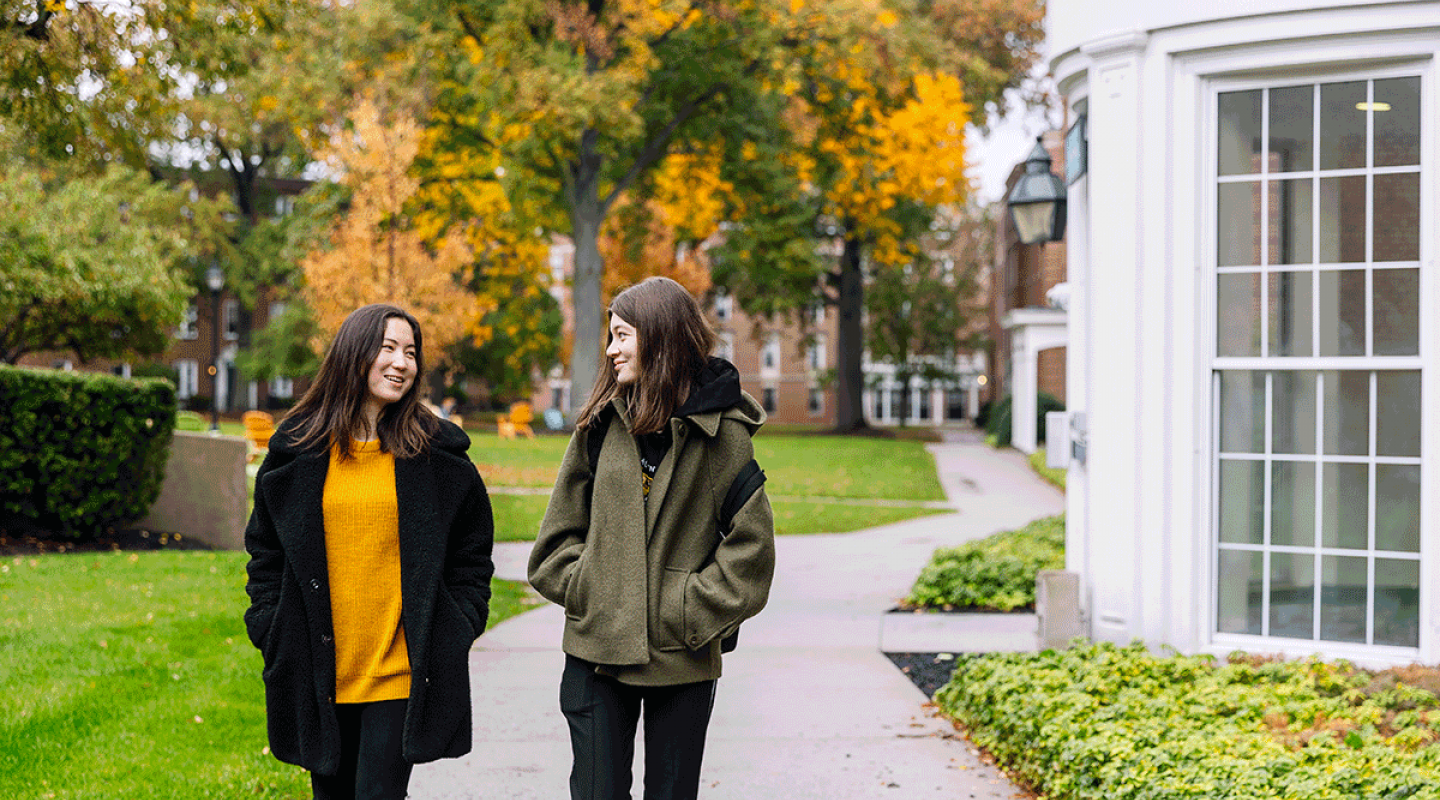 Two Simmons students walking and talking on a campus path