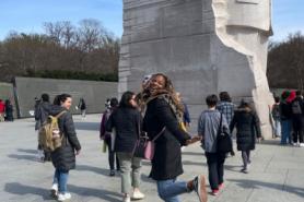 Student smiling in front of Dr. Martin Luther King, Jr. statue during Alternative Spring Break