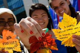 A group of three students holding up colorful fall leaves with their aspirations written on them