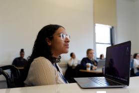 A Simmons student listening attentively during a class.  A laptop is open on the desk in front of the student.