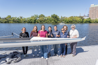 Current and former members of the Simmons rowing program gathered together on the dock of the Riverside Boat Club with a new shell