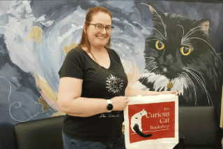 Stacy Whitman stands in fron of a mural holding a bag from her bookshop The Curious Cat