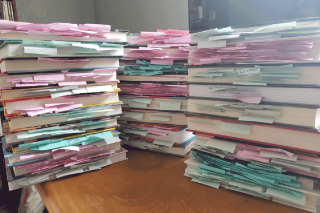 Three piles of books with sticky notes hanging out between the pages.