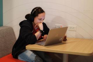 A Simmons student seated in a booth concentrating on their laptop screen