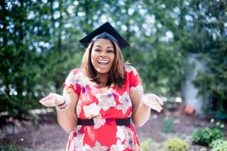 A student wearing a graduation cap, shrugging their shoulders and holding their palms up as if asking a question