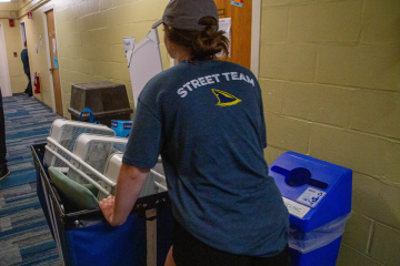 A member of the Simmons Street Team pushing a cart full of belongings down the hallway of a residence hall