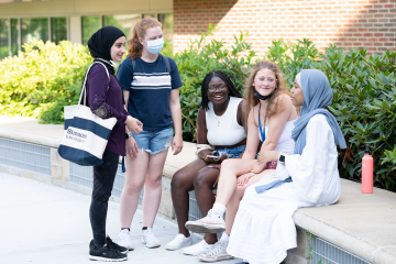 A group of Simmons students having a conversation while some are seated on a low patio wall 