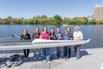 Current and former members of the Simmons rowing program gathered together on the dock of the Riverside Boat Club with a new shell