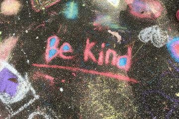 The words Be Kind written among several photos drawn in chalk on pavement