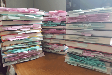 Three piles of books with sticky notes hanging out between the pages.