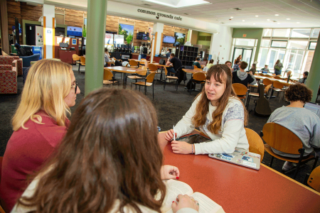 Students have a conversation at tables near the Common Grounds Cafe