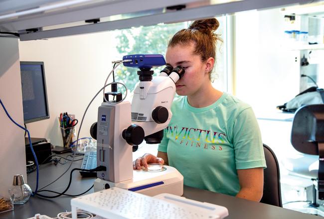 A Simmons University student using a high-powered microscope in the Science Center