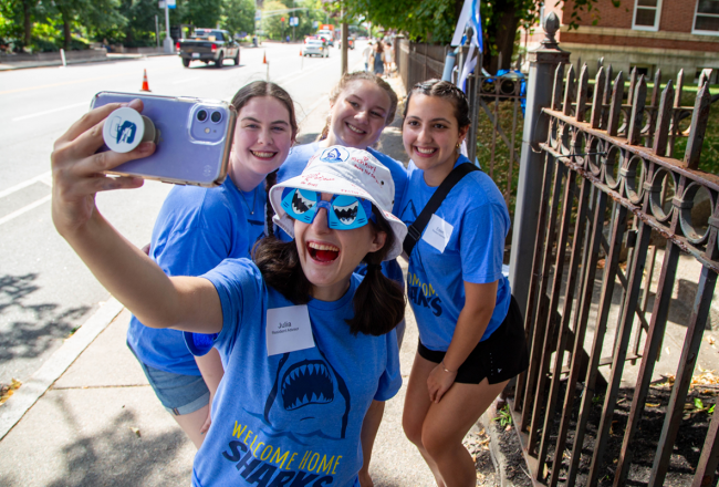 A group of residence advisors pose for a selfie wearing "Welcome Home Sharks" shirts