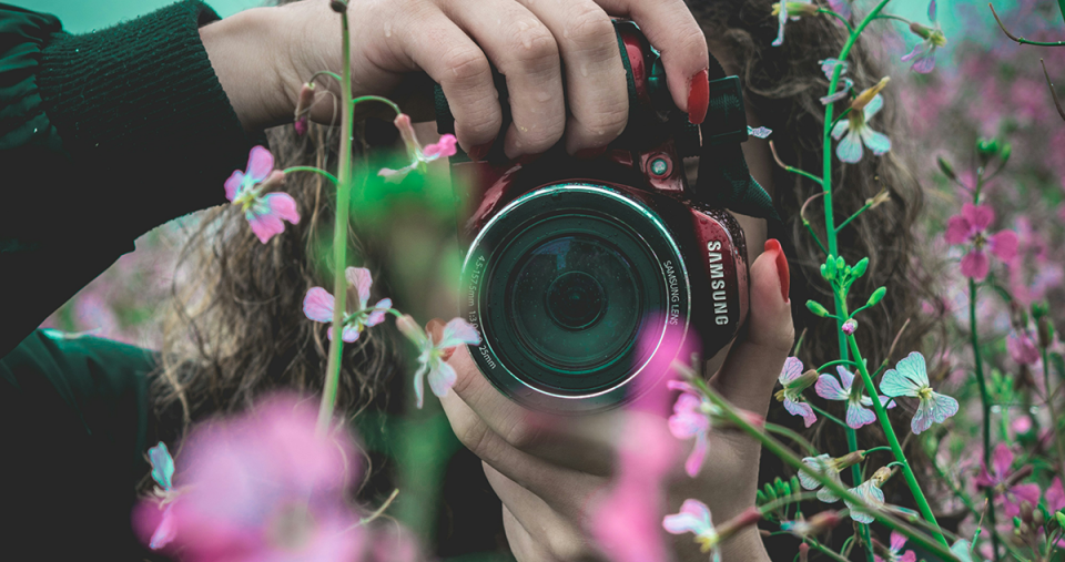 A photographer pointing a camera through some flowers