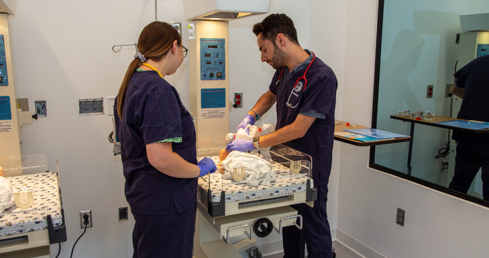 Two nursing students work with the infant simulator