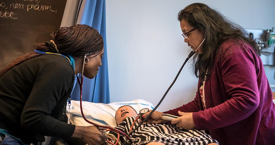 Two nursing students perform an exam on a nursing mannequin