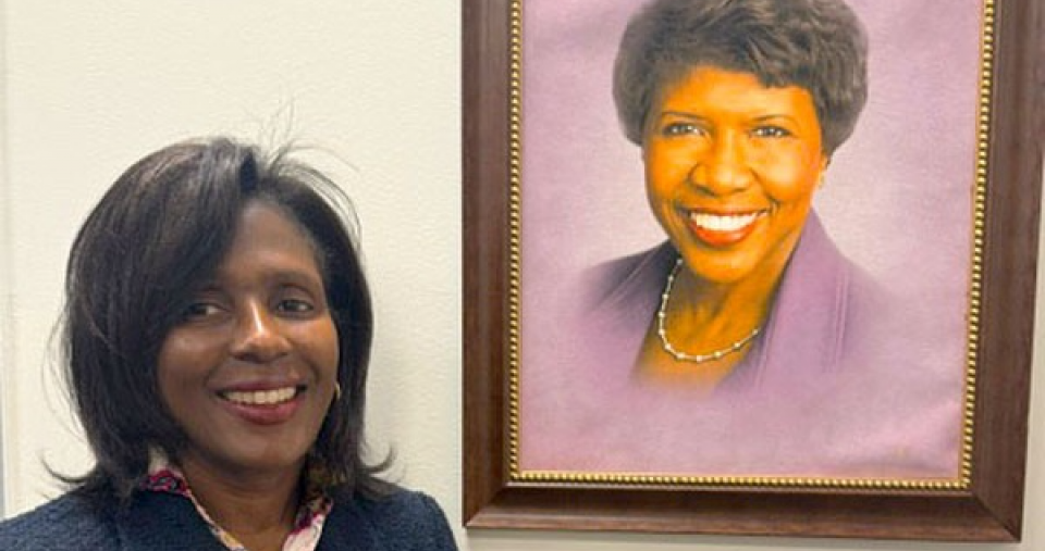 Simmons President Lynn Perry Wooten standing near a portrait of Gwen Ifill