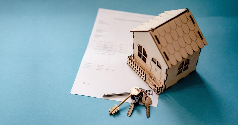 Image of small model of house sitting on paper. Set of keys next to it.